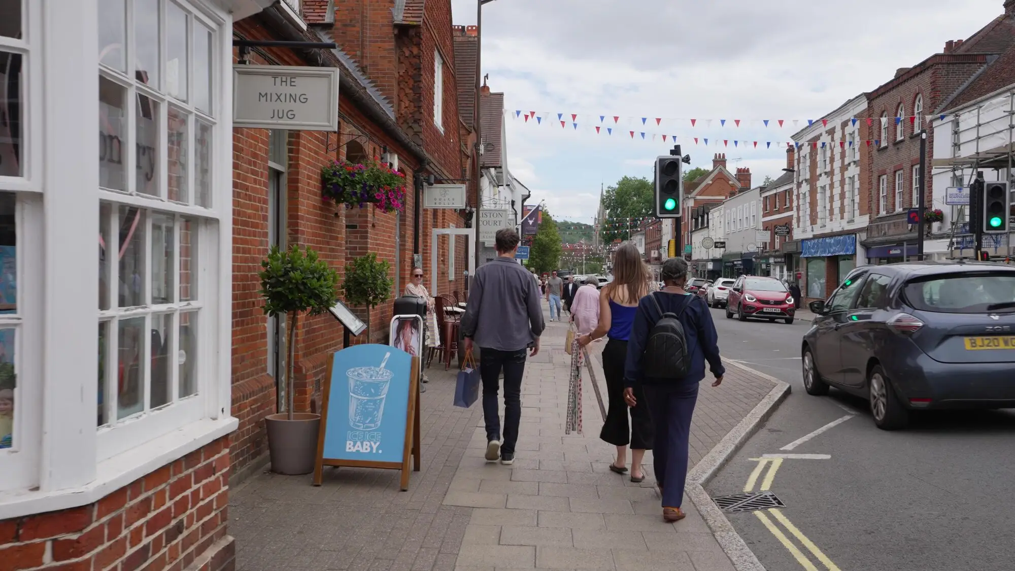 Shoppers walking along Marlow High Street past brick shopfronts and bunting.